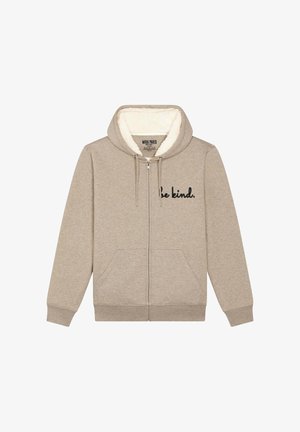 Khaki színű, zipzáras kapucnis pulóver puha, krém színű béléssel. Elöl zsebekkel rendelkezik, és a bal mellrészen fekete hímzéssel van feliratozva: "légy kedves."