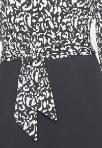 Top envolvente de patrón en blanco y negro con un detalle de lazo en la cintura, confeccionado en una tela suave con una ligera textura de caída.