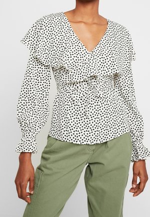 Witte blouse met zwarte hartprint, gerimpelde V-hals, lange pofmouwen met gerimpelde manchetten, taille gestrikt, gecombineerd met lichtgroene broek.