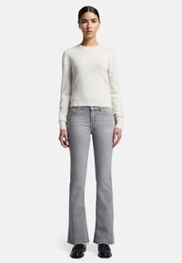 Lys grå, flagrende jeans kombineret med en kremfarvet, tætsiddende bluse med lange ærmer. Jeansene har en rå kant og en subtil lysning.