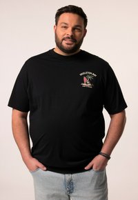 Sort t-shirt med korte ærmer, der har et farverigt grafisk design af et surfbræt og en palme i venstre brystområde, parret med lyseblå jeans.