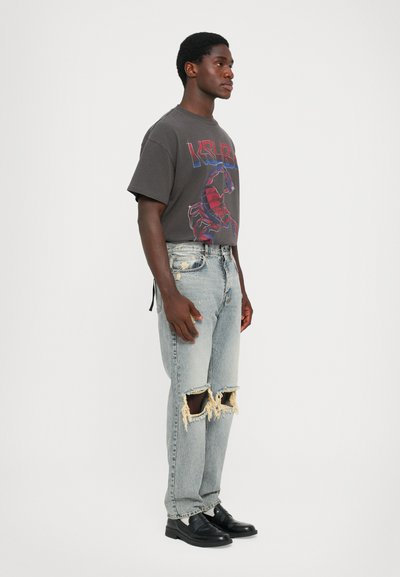 Tricou gri cu un design roșu și albastru, asortat cu blugi ușor albaștri, distruși, cu genunchi rupti. Pantofi negri completează ținuta.
