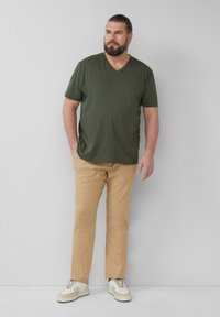 Donkergroene T-shirt met korte mouwen en V-hals, beige rechte broek en witte sneakers met beige accenten. Eenvoudig ontwerp en comfortabele pasvorm.