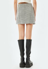 Minigonna houndstooth bianca e nera con taglio dritto, dotata di zip sul retro e finitura in tessuto liscia, abbinata a stivali neri fino al ginocchio.
