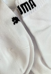 Weiße Baumwollsocken mit gerippten Bündchen. Eine Socke hat einen schwarzen Akzent mit dem Wort "ima" und einem kleinen schwarzen Herzen. Glatte Textur.