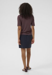 Kortærmet brun top sat sammen med en marineblå nederdel, der har et enkelt design. Outfittet suppleres af sko med gennemsigtige hæle.