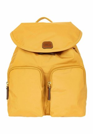 Sac à dos jaune avec deux poches zippées à l'avant, tirettes de fermeture éclair en cuir, rabat supérieur et petite pièce en cuir avec le nom de la marque "BRICS" sur le devant.