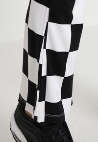 Black and white checkered pants made from stretchy fabric with a smooth texture, featuring a fitted cut and contrasting stitching details.