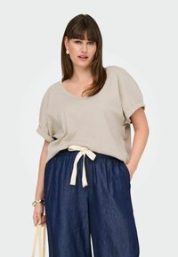 Beige ribbet top med bred udskæring og opremsede ærmer, parret med mørk denim bukser med brede ben og en crema bånd i taljen.