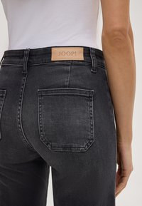 Zwarte denim jeans met een gladde textuur, voorzien van een leren label "JOOP!" op de tailleband en twee achterzakken.