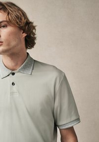 Hellgraues Poloshirt mit einem strukturierten Kragen mit geometrischem Muster, kurzen Ärmeln mit gemusterten Bündchen und drei schwarzen Knöpfen.