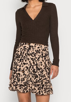 Femme portant un haut à manches longues côtelé marron foncé avec col en V et une jupe beige avec imprimé animal noir et marron et des détails à volants.