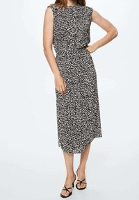 Robe midi à motifs noir et blanc avec des manches courtes, décolleté froncé et taille cintrée. Portée avec des sandales noires à lanières.