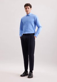 Lichtblauw overhemd met lange mouwen, een puntige kraag, knoopsluiting aan de voorkant, gecombineerd met op maat gemaakte donkere broek en zwarte veterschoenen.