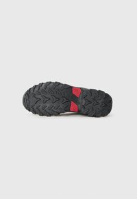 Semelle de chaussure de course en trail avec un design en caoutchouc noir robuste, des crampons profonds pour l'adhérence et un accent rouge dans la zone du talon pour la stabilité.