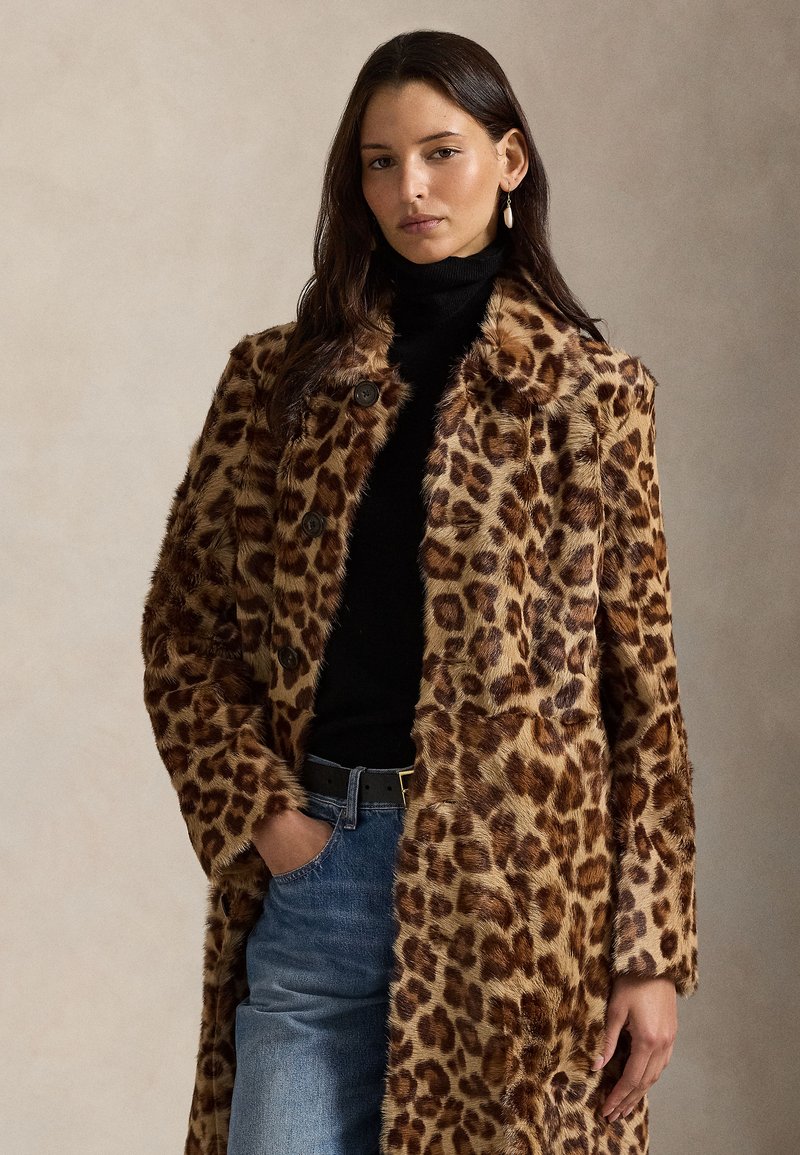 Kabát z umelého kožušinového materiálu s leopardím vzorom, s výstrihom do špica, gombíkmi a bočnými vreckami, skombinovaný s čiernym rolákom a modrými džínsami.