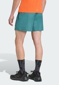 Teal running shorts with a lightweight fabric, elastic waistband, and side pockets; worn with dark gray compression socks and black sneakers.