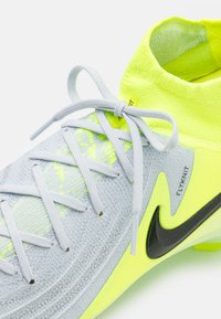 Scarpa sportiva grigio chiaro con accenti gialli brillanti. Presenta una tomaia in maglia, chiusura con lacci e il logo Nike Swoosh nero.