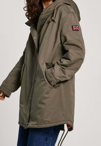 Oliwkowa parka z kapturem, z zamkiem błyskawicznym z przodu, kieszeniami po bokach oraz naszywką z brytyjską flagą na rękawie. Teksturowany materiał.