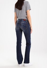 Ciemnoniebieskie jeansy o prostych nogawkach z efektem sprania, przeszywanymi tylnymi kieszeniami i skórzaną metką na pasku. W połączeniu z koszulką w paski.