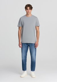 Szara bawełniana koszulka z okrągłym dekoltem, krótkimi rękawami, zestawiona z niebieskimi dżinsami i białymi trampkami. Prosty, dopasowany fason bez wzorów.