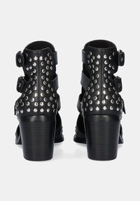 Botines negros con un diseño de tachuelas, lados abiertos y correas ajustables, y un tacón grueso para mayor estabilidad.