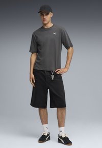 Camiseta de algodón gris con mangas cortas, combinada con pantalones cortos de mezclilla negros. Se lleva con calcetas blancas y zapatillas negras, acentuado por detalles en plata.