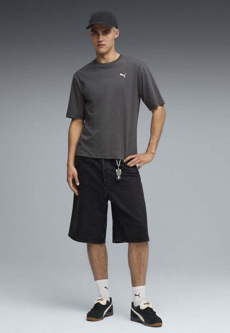 Camiseta de algodón gris con mangas cortas, combinada con pantalones cortos de mezclilla negros. Se lleva con calcetas blancas y zapatillas negras, acentuado por detalles en plata.