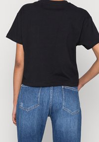 Svart croppad t-shirt i bomull, med korta ärmar och rund halsringning, ihop med höga blå denimjeans med två bakfickor.