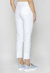 Białe spodenki o prostym kroju, z gładką fakturą, dwiema tylnymi kieszeniami oraz wzmocnionym dołem. W zestawieniu z jasnoniebieskimi trampkami.