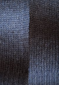 Gros plan sur un tissu tricoté avec des rayures verticales alternées en gris foncé et bleu, montrant la texture duveteuse et les détails du fil.