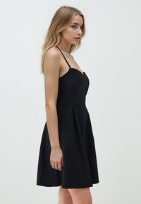 Zwarte A-lijn jurk met dunne bandjes, sweetheart halslijn, getailleerd lijfje en uitlopende rok. Glad materiaal, minimalistisch ontwerp, kniehoogte.