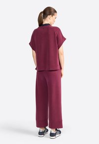 Oversized kastanjebruine sweatshirt met korte mouwen gecombineerd met wijde broekspijp. Heeft een gestructureerde hals en unieke achterkantdetails. Casual schoeisel inbegrepen.