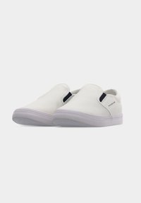 Paire de chaussures en toile blanches sans lacets avec semelles en caoutchouc blanches et panneaux latéraux élastiques sur un fond uni.
