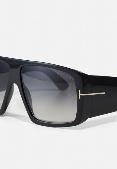 Sorte oversized solbriller med gradient linser, glat plastiske stel og detalje i guldfarve på brillestængerne.