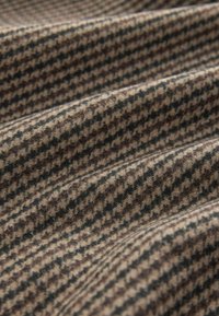 Houndstooth raštas audinys rudos ir juodos spalvų, turintis minkštą, tekstūruotą paviršių su matomomis raukšlėmis ir sukabėjimais.