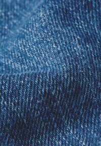 Primo piano di un tessuto in denim blu che mostra la dettagliata trama intrecciata e i modelli di cucitura con diverse sfumature di blu e fibre bianche.