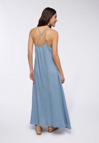 Lungo abito maxi blu senza maniche con schiena arricciata e spalline incrociate. Texture liscia e silhouette fluida per facilità di movimento.