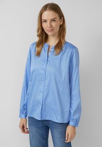 Camicia azzurra chiaro con bottoni realizzata in tessuto morbido, con colletto, maniche lunghe con polsini elastici e una vestibilità rilassata.