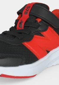 Μαύρο και κόκκινο αθλητικό παπούτσι New Balance με λευκή σόλα, μαύρα κορδόνια και κόκκινη λουρί Velcro με την ένδειξη 578 στη γλώσσα.