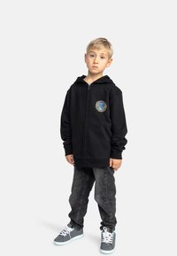 Černá mikina na zip s vícebarevným logem, spárovaná s tmavě šedými džíny a šedými teniskami s bílými tkaničkami; neformální, uvolněný střih.