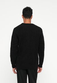 Schwarzer gestrickter Pullover mit strukturierten Mustern, Rundhalsausschnitt und langen Ärmeln. Das Design umfasst erhabene Details über den gesamten Stoff.