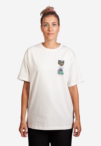 T-shirt bianco in cotone con maniche corte, caratterizzato da una stampa grafica sul petto in colori vivaci. Vestibilità rilassata e colletto tondo.