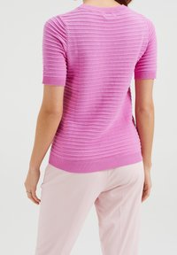 Kortärmad, ribbad rosa tröja med rund halsringning och en figurnära siluett. Texturen har horisontella ränder. Kombinerad med ljusrosa byxor.