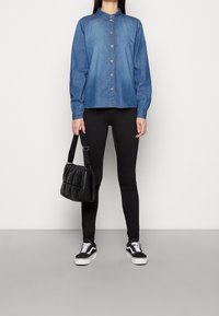 Denim button-up shirt with a collar, long sleeves, and a solid blue color. Paired with black skinny jeans and a black textured handbag.