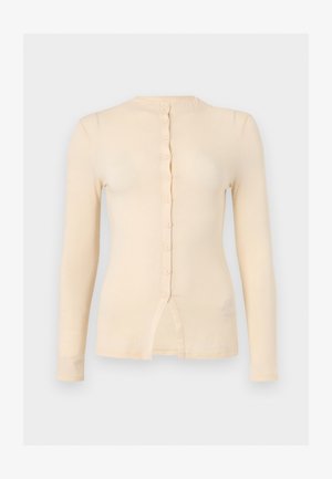 Top bej cu mânecă lungă, croială mulată, cu decolteu rotund, nasturi în față și o mică despicătură în partea de jos, în centru.