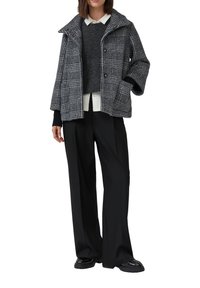 Szary i czarny płaszcz w kratę z dużym kołnierzem, zapięciem na guziki oraz dwoma przednimi kieszeniami, połączony z ciemnym swetrem i czarnymi szerokimi spodniami.