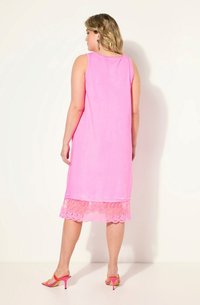 Robe sans manches rose avec une bordure en dentelle, présentant une texture lisse. Associée à des sandales à talons multicolores.