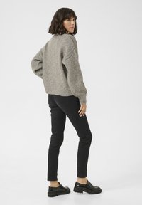 Grau gestrickter Pullover mit überschnittenen Schultern und ribbed Saum, kombiniert mit schwarzen, engen Jeans und schwarzen klobigen Schuhen. Sichtbare Rückansicht.