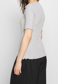Camiseta gris ajustada con textura acanalada, mangas cortas con volantes y escote redondeado, usada sobre una falda negra.